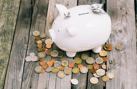 Skarbonka świnka i rozsypane monety obrazujące program oszczędnościowy