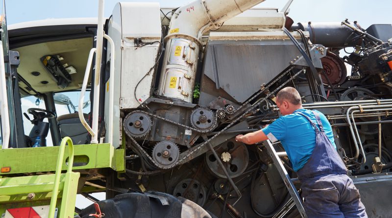 Pracownik serwisu maszyn drogowych naprawiający podzespół silnika w dużej maszynie roboczej na zewnątrz.